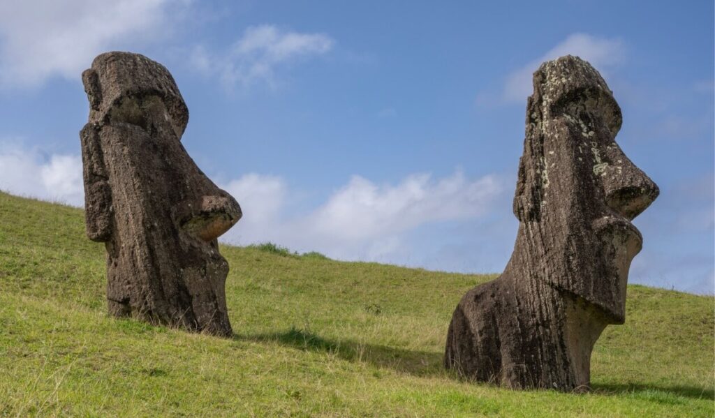 Due statue Moai in pietra parzialmente sepolte su un pendio erboso a Rapa Nui, Isola di Pasqua.